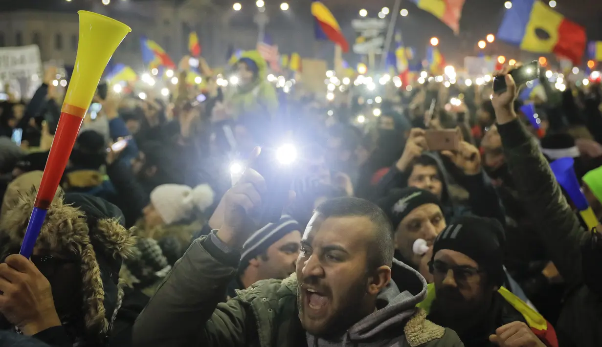 Pengunjuk rasa berkumpul di pusat Bucharest sambil melambai-lambaikan bendera, Rumania, Minggu (5/2). Mereka bersorak mendengar pengumuman yang dikeluarkan setelah unjuk rasa selama hampir 1 minggu. (AP Photo)
