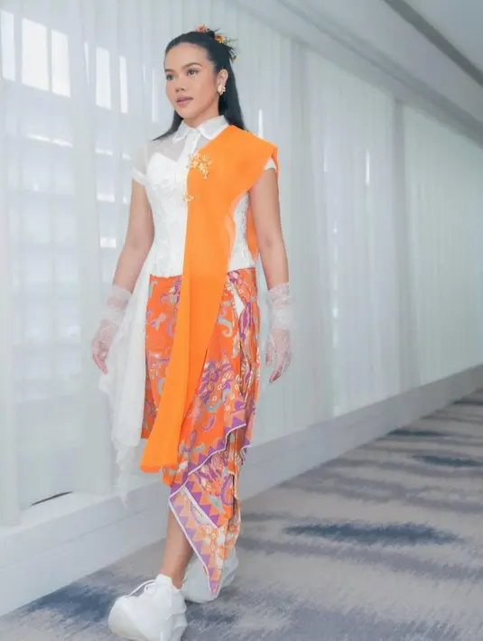Yura Yunita selalu memodifikasi tampilan tradisional menjadi lebih modern. Misalnya saja, ia mengenakan atasan putih berkerah dengan bustier bersiluet kebaya dipadukan selendang orange senada dengan bawahan kain batiknya. [@yurayunita]