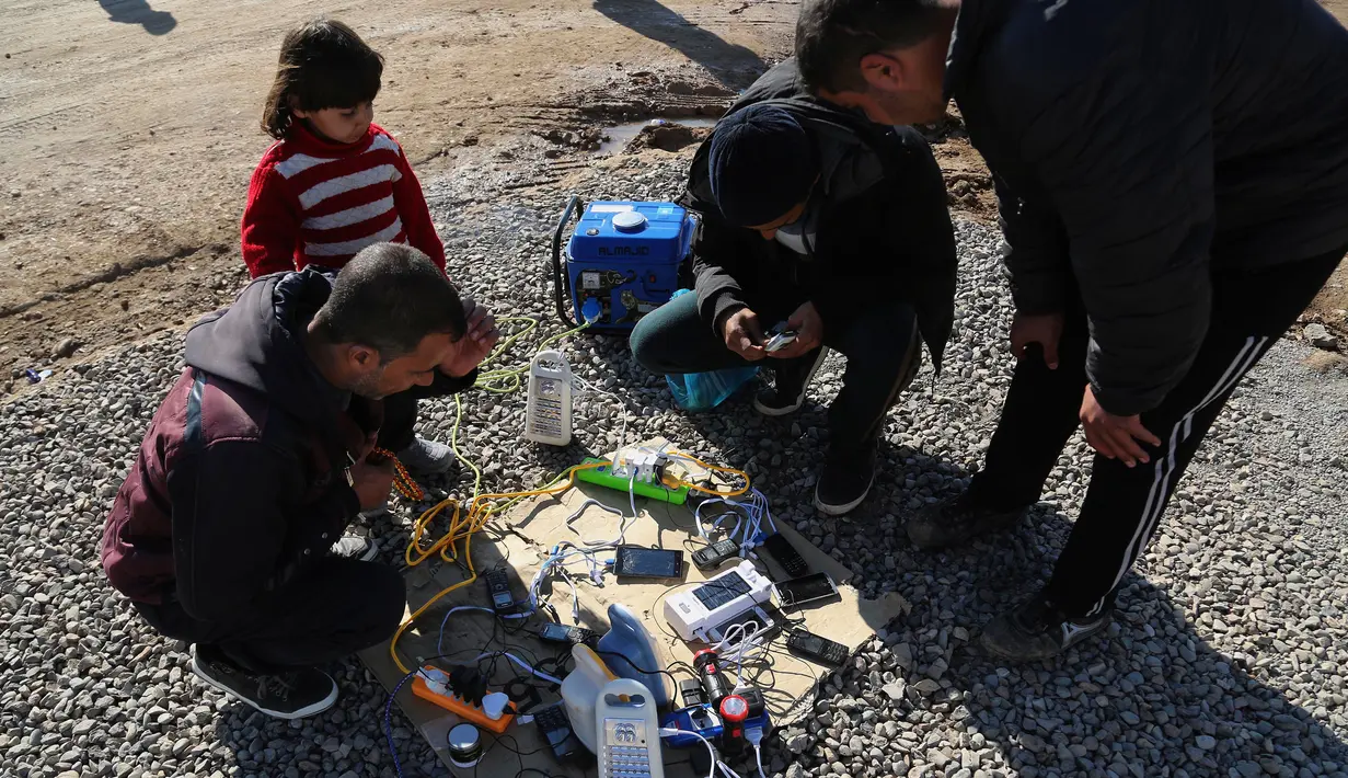 Warga yang melarikan diri dari pertempuran antara pasukan Irak melawan kelompok ISIS mengisi baterai ponselnya di kamp pengungsian Sewdinan, Khazer, Irak, (3/1). Pengisian baterai setiap ponsel dikenakan biaya 500 dinar Irak. (AP Photo / Khalid Mohammed)