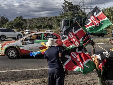 Pembalap Italia, Riccardo Garosci memacu mobilnya, Mitsubishi Lancer Evo X bersama co-driver Rudy Briani melewati pedagang bendera Kenya dan vuvuzelas saat Safari Relly Kenya di Naivasha, Kenya, 28 Maret 2024. (AFP/Luis Tato)