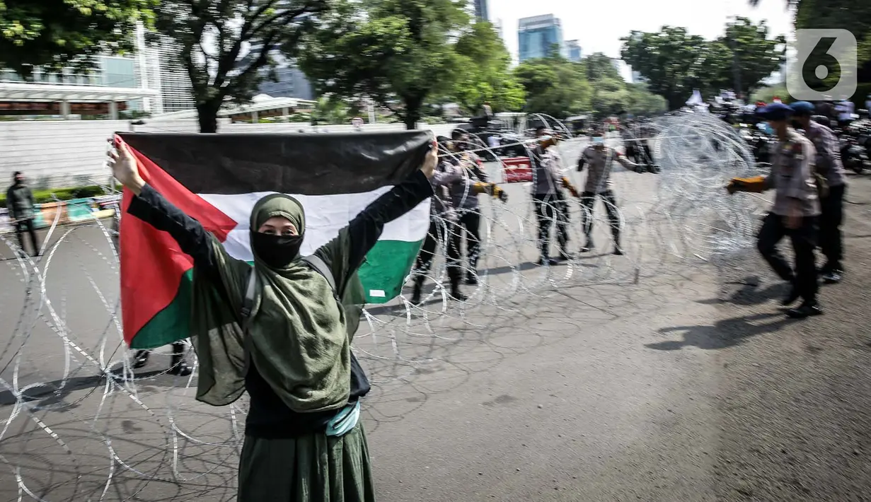 Seorang wanita mengibarkan bendera Palestina saat polisi memasang kawat berduri dalam aksi solidaritas untuk rakyat Palestina di Depan Kedutaan Besar Amerika Serikat, Jakarta (18/5/2021). Massa mengutuk dan mengecam keras kekerasan yang dilakukan Israel atas Palestina. (Liputan6.com/Faizal Fanani)