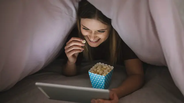 Seorang Wanita Sedang Menonton Film di Tablet Sambil Memakan Popcorn