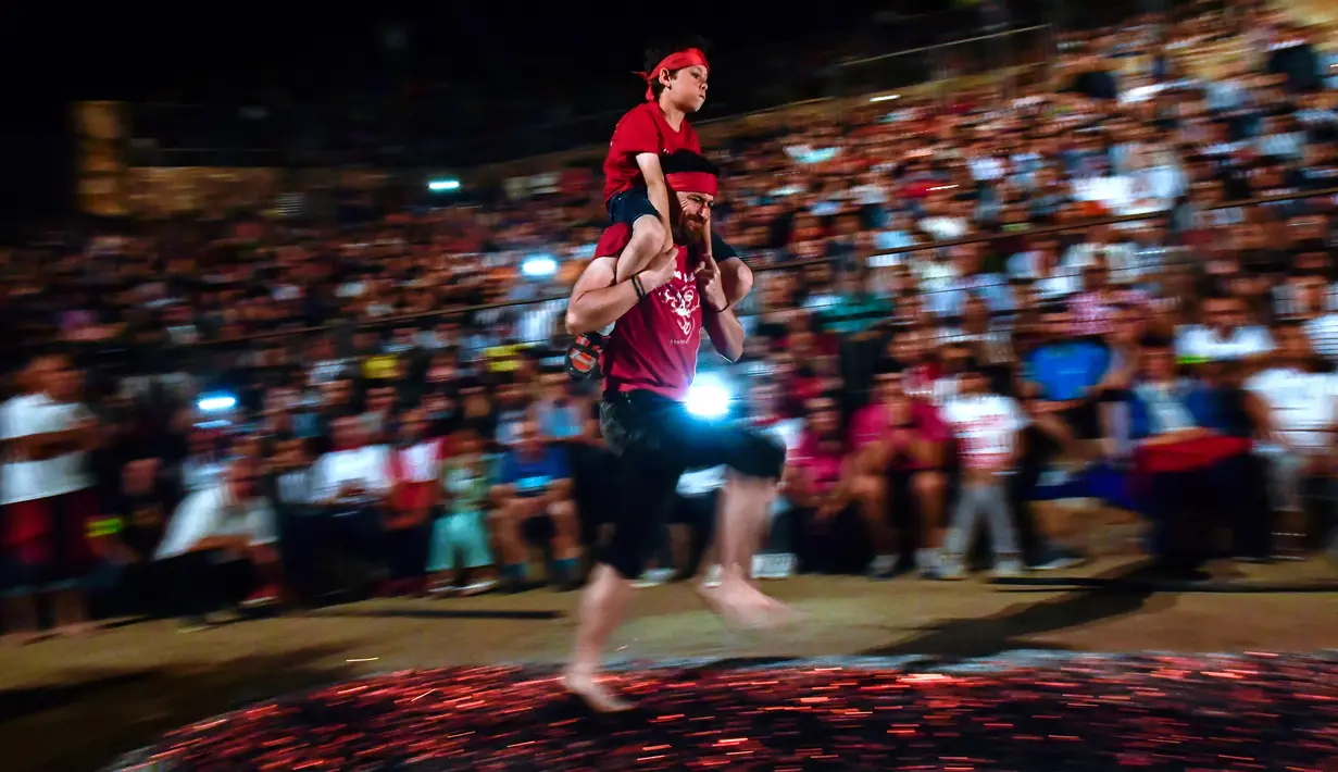 Seorang pria membawa anak lelaki di punggungnya sambil berjalan di atas bara api selama malam San Juan di San Pedro Manrique, Spanyol Utara, Minggu (24/6). Tradisi kuno Spanyol ini diperingati untuk menyambut musim panas. (AP Photo/Alvaro Barrientos)