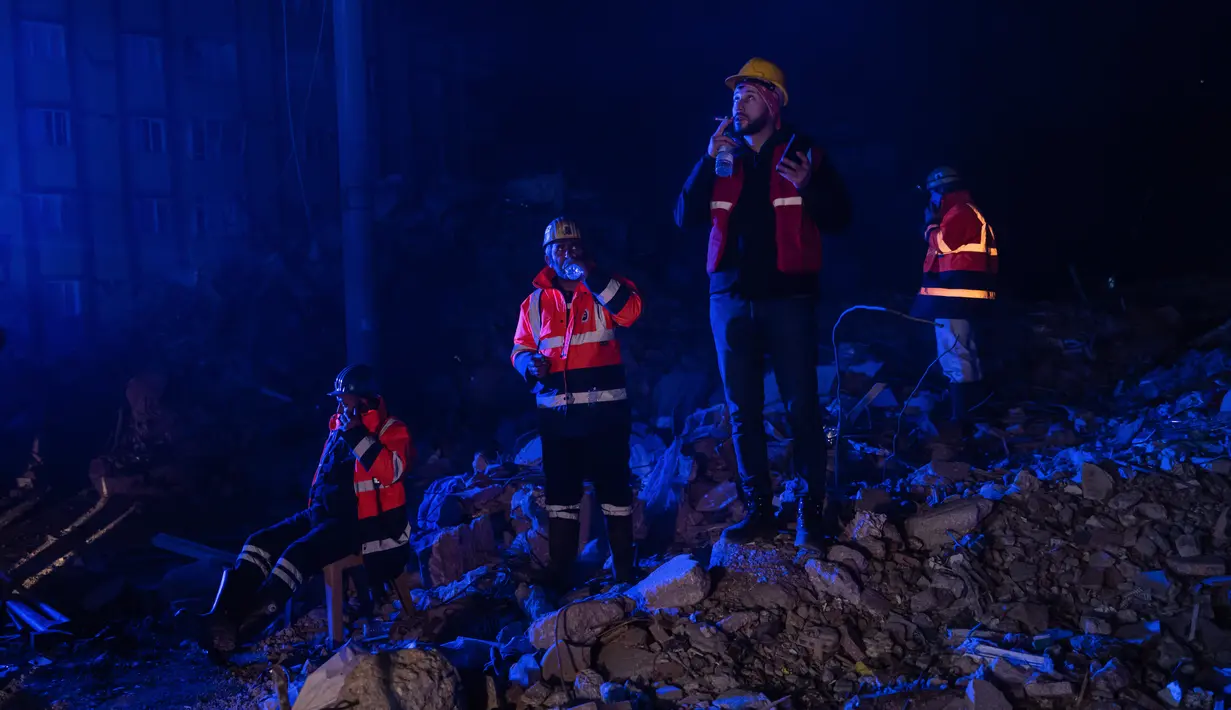 Petugas penyelamat beristirahat saat yang lain mencari korban di bangunan yang runtuh setelah gempa berkekuatan 6,4 SR kedua melanda provinsi Hatay di selatan Turki, di Antakya, pada 20 Februari 2023, dua minggu setelah gempa berkekuatan 7,8 SR. Dalam sebuah pernyataan, Menteri Dalam Negeri Turki Suleyman Soylu mengonfirmasi tiga orang tewas dan lebih dari 200 orang terluka akibat gempa pada Senin tersebut. (AFP/Sameer Al-Doumy)