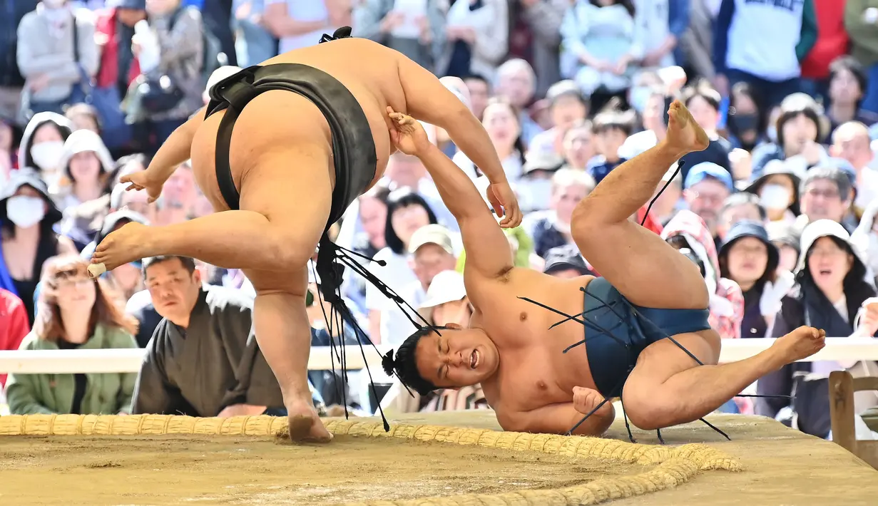 Pegulat sumo membanting lawannya saat bertanding dalam turnamen Honozumo di Kuil Yasukuni, Tokyo, Jepang, 15 April 2019. Turnamen ini digelar setiap tahun. (TRIBALLEAU CHARLY/AFP)