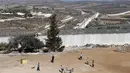 Suasana saat anak-anak bermain sepak bola di samping tembok pemisah Israel - Palestina di desa Beit Awa di Tepi Barat yang diduduki Israel (12/11). (AFP Photo/Hazem Bader)