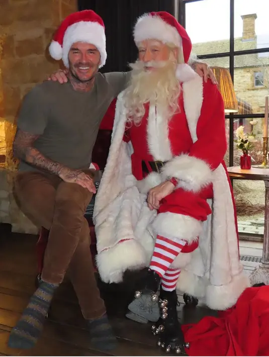 Sambil merangkul Santa Claus, David mengenakan atasan kaos dipadukan celana coklat dan kaos kakinya. Ia juga mengenakan topi Santa. [@victoriabeckam]