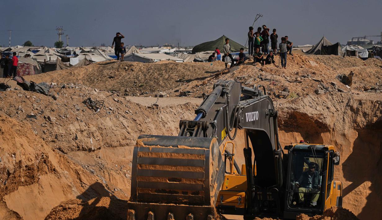 Warga Palestina menyaksikan aktivitas pekerja Mesir yang menggunakan alat berat untuk mencari jenazah para sandera di Kota Hamad, Khan Younis, di Jalur Gaza selatan, Selasa 28 Oktober 2025. Di Khan Younis, proses penggalian tanah terlihat menggunakan alat berat di tengah reruntuhan. (AP Photo/Abdel Kareem Hana)