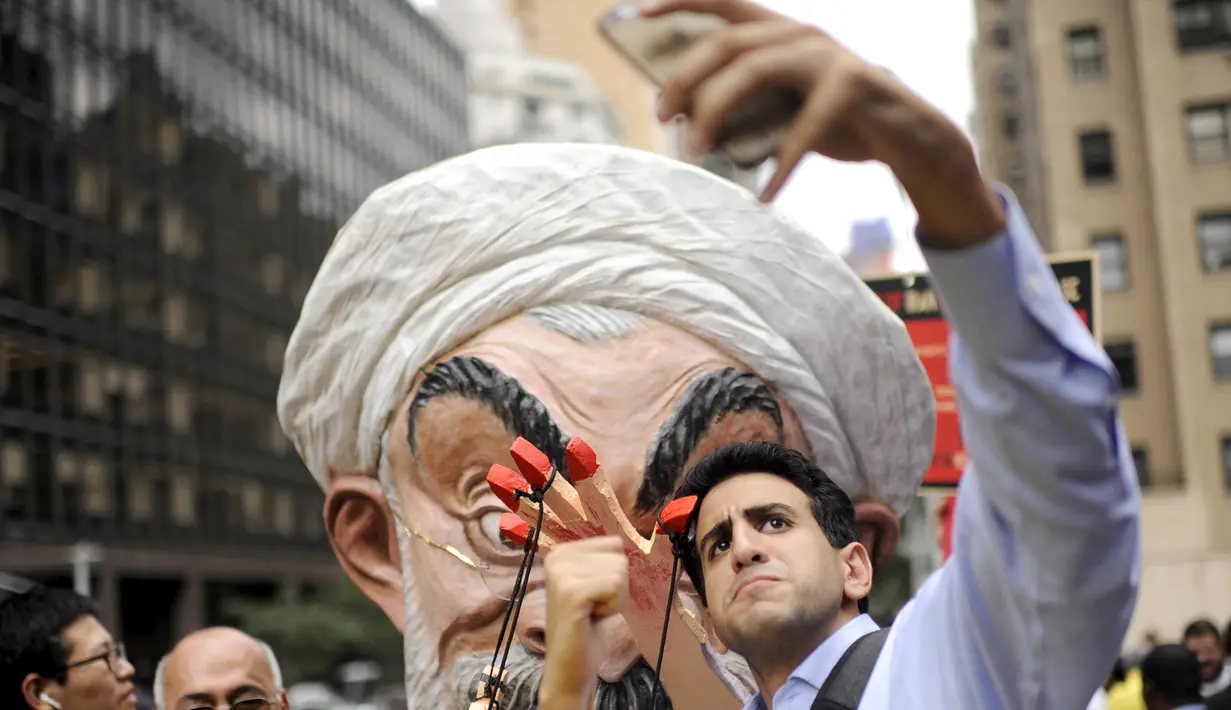Seorang pria berselfie dengan Max Saatchi yang memakai topeng Presiden Iran Hassan Rouhani mengecam pelanggaran hak asasi manusia oleh pemerintah Rouhani di luar markas besar PBB, Manhattan, New York, AS (28/9/2015). (REUTERS/Darren Ornitz)