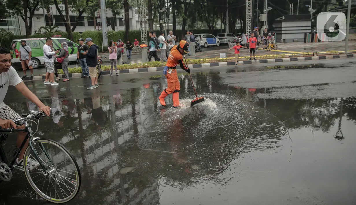 Petugas Penanganan Prasaran dan Sarana Umum (PPSU) membersihkan genangan air saat car free day (CFD) di kawasan Bundaran HI, Jakarta, Minggu (29/12/2019). Pembersihan genangan air dilakukan agar warga yang sedang berolahraga di kawasan tersebut nyaman. (Liputan6.com/Faizal Fanani)