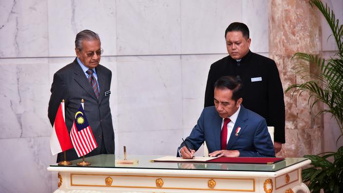 Presiden Joko Widodo menandatangani dokumen disaksikan Perdana Menteri Malaysia Mahathir Mohamad di Putrajaya (8/8/2019). Pertemuan juga membahas masalah WNI di Malaysia hingga kelapa sawit dan kedua pemimpin tersebut akan Salat Jumat bersama. (Farhan Abdullah/Department Of Information/AFP)