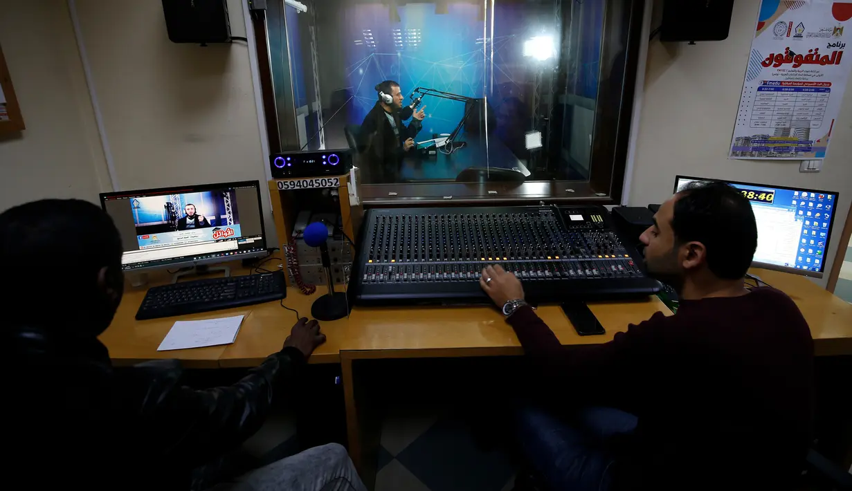 Teknisi membantu guru yang melakukan siaran di sebuah stasiun radio pendidikan di Jalur Gaza, Palestina, Minggu (15/3/2020). Di tengah kebijakan isolasi untuk mencegah penyebaran virus corona COVID-19, guru di Jalur Gaza menyampaikan materi pelajaran melalui siaran radio. (MOHAMMED ABED/AFP)