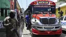 Seorang tentara berjalan di depan sebuah bus di Comasagua, El Salvador, Senin (3/10/2022). Pengepungan besar-besaran kota Comasagua adalah contoh terbaru dari taktik keras pemerintah untuk membasmi geng jalanan. Setiap orang yang memasuki atau meninggalkan kota ditanyai atau digeledah. (AP Photo/Salvador Melendez)