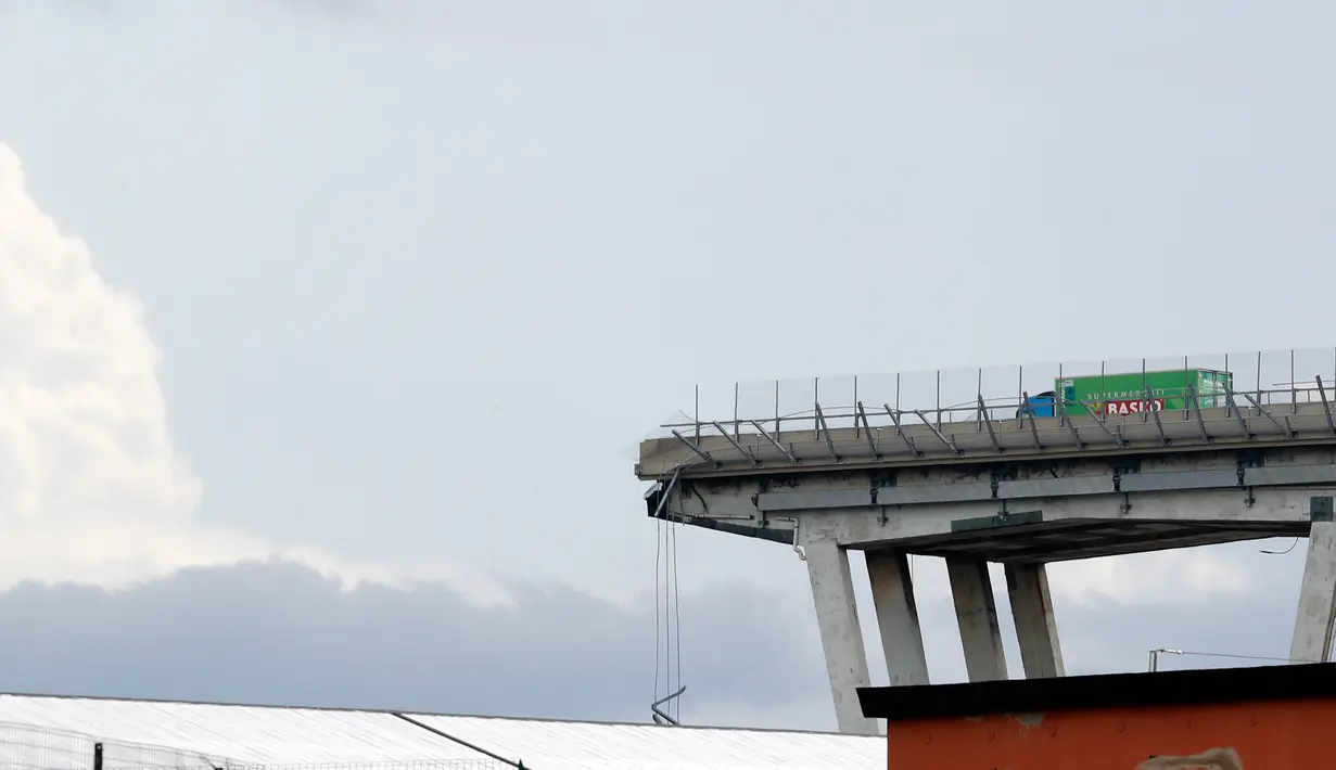Sebuah truk berada di atas jembatan Morandi, dekat dengan bagian jalan layang yang runtuh, di Genoa, italia, Selasa (14/8). Sekitar 300 petugas pemadam kebakaran dan tim penyelamat diterjunkan ke lokasi untuk menemukan korban selamat. (AP/Antonio Calanni)