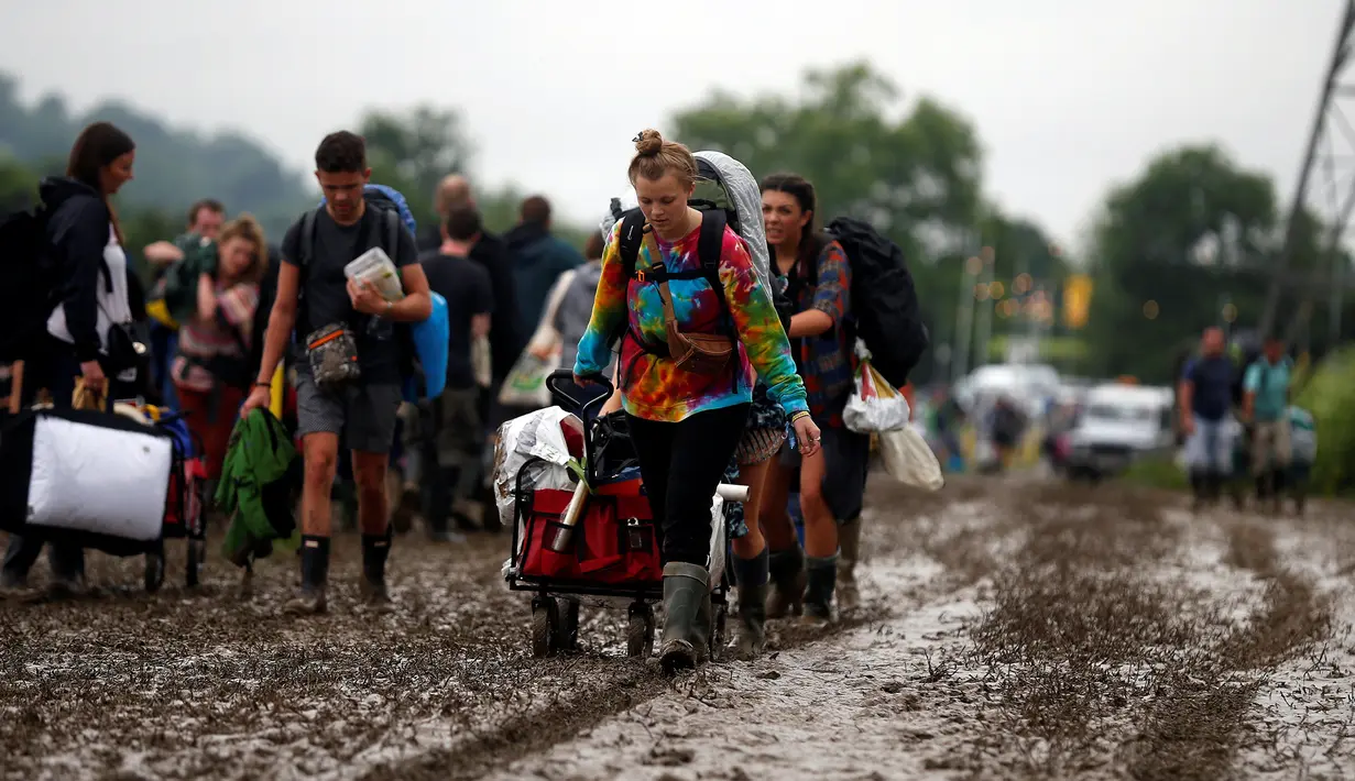 Penonton Festival Glastonbury membawa barang-barang mereka melewati jalanan yang banjir dan berlumpur saat tiba di Worthy Farm, Somerset, Inggris, (22/6). Di gelaran ke-34 kali ini akan menghadirkan musisi-musisi hebat dunia. (REUTERS / Stoyan  Nenov)