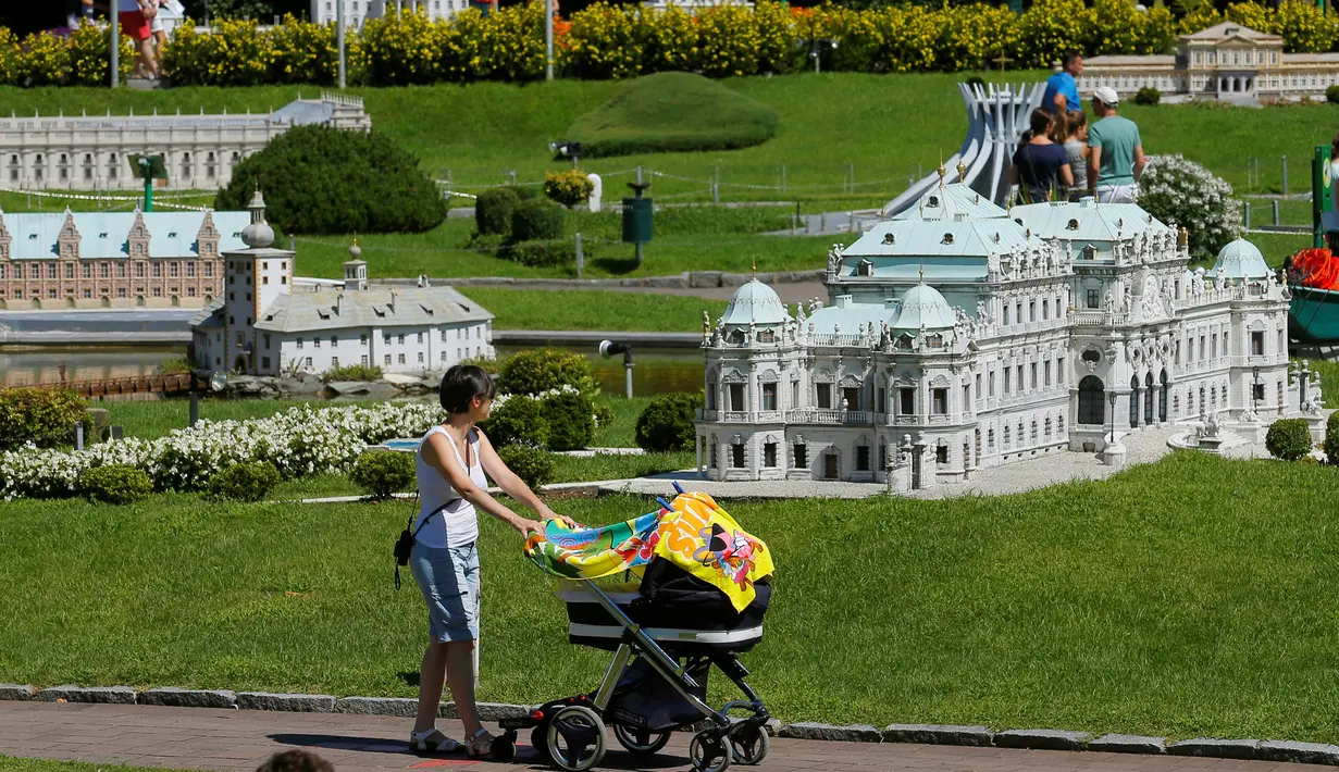 Pengunjung sambil mendorong kereta bayi melihat miniatur Wina Belvedere Palace di Taman Minimundus, Klagenfurt, Austria, Senin (8/8). Sekitar 150 model bangunan unik dari berbagai belahan dunia dipamerkan di Taman Minimundus. (REUTERS / Heinz-Peter Bader)