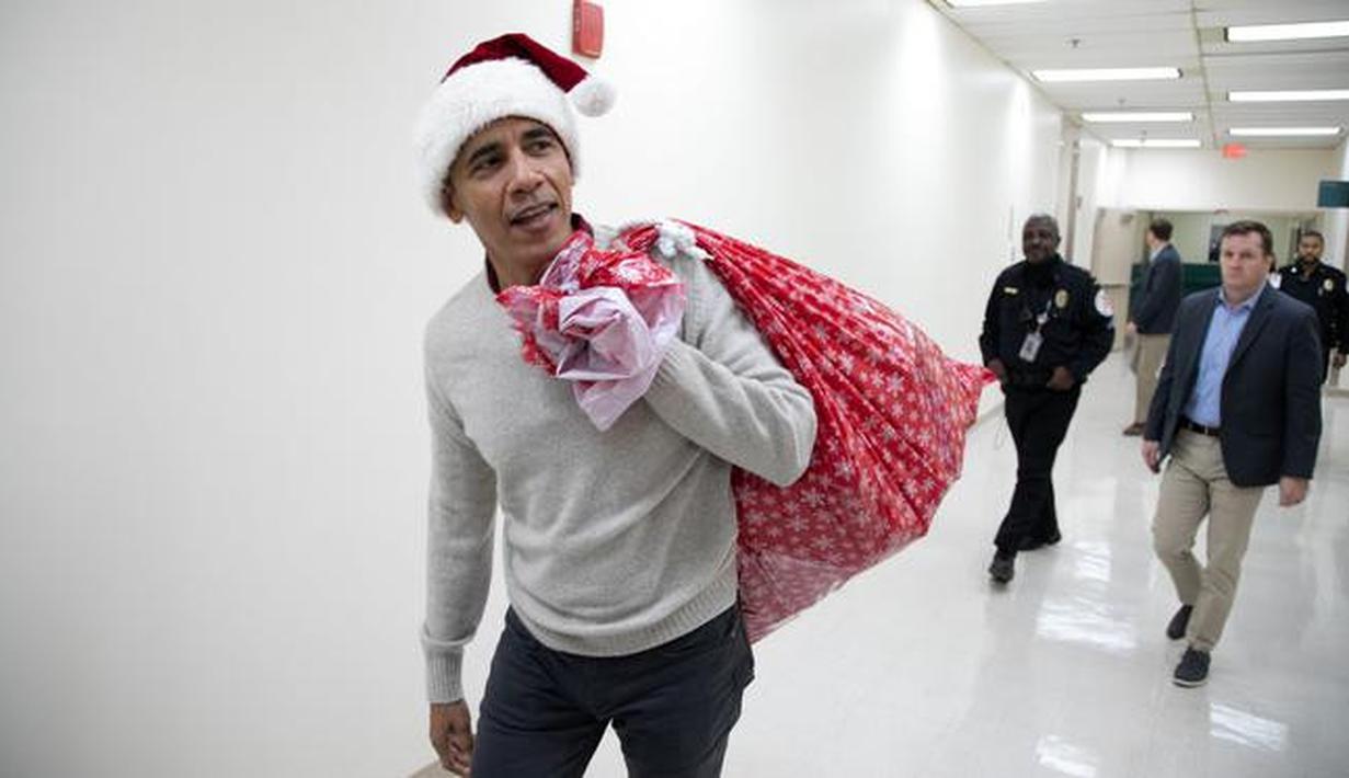 Mantan Presiden AS, Barack Obama mengunjungi Children's National Medical Center di Washington, Rabu (19/12). Dengan topi khas merah putih ala sinterklas, Obama membagikan hadiah natal untuk anak-anak yang sedang menjalani perawatan. (Chuck Kennedy / AFP)