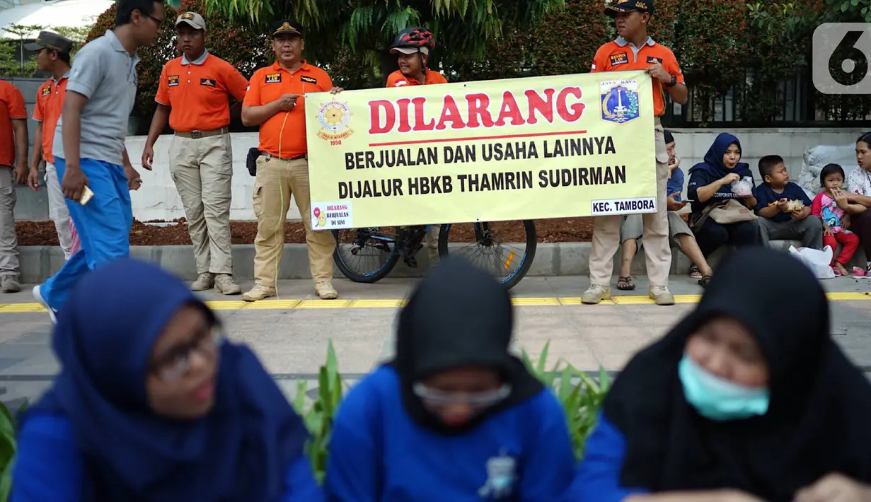 Spanduk larangan berjualan yang dibentangkan petugas Satpol PP di jalur Hari Bebas Kendaraan Bermotor atau Car Free Day, Jakarta, Minggu (3/11/2019). Pemprov DKI melarang PKL berjualan di sepanjang jalur Car Free Day yang selama ini memenuhi jalan serta trotoar. (Liputan6.com/Immanuel Antonius)