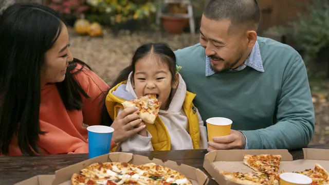 Seorang anak perempuan sedang menikmati pizza bersama kedua orang tuanya (Foto Dok: Freepik/freepik)