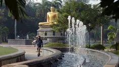 Seorang pria berjalan di depan patung Buddha di Taman Viharamahadevi di Kolombo, Sri Lanka (3/1). Taman tertua dan terbesar dari Pelabuhan Kolombo, terletak di depan gedung Balai Kota bergaya kolonial. (AFP Photo/Lakruwan Wanniarachchi)