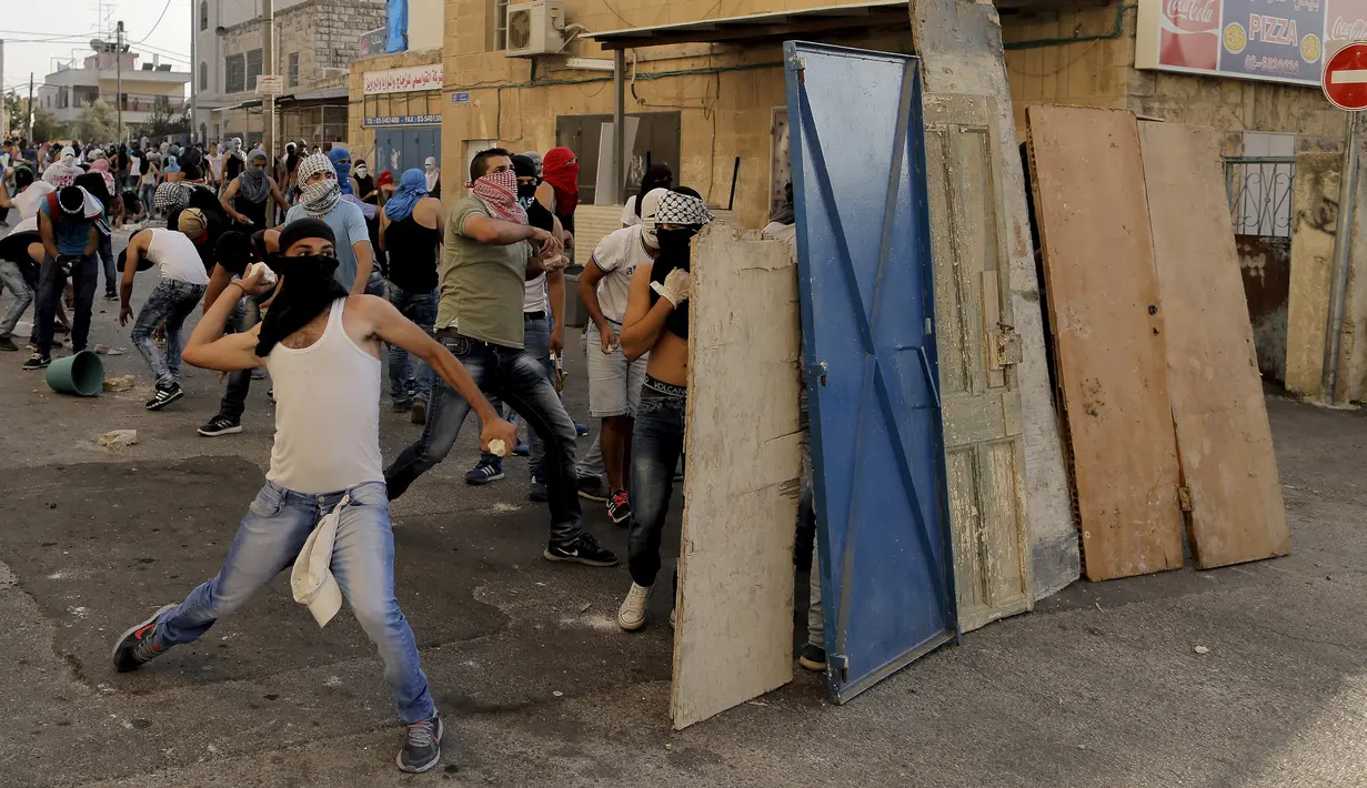 Warga Palestina melempar batu ke arah polisi Israel dalam bentrokan di Shuafat, sebuah daerah pinggiran Arab, Yerusalem, Senin (5/10/2015). Seorang remaja Palestina tewas pada Senin dalam bentrokan di Tepi Barat. (REUTERS/Ammar Awad)