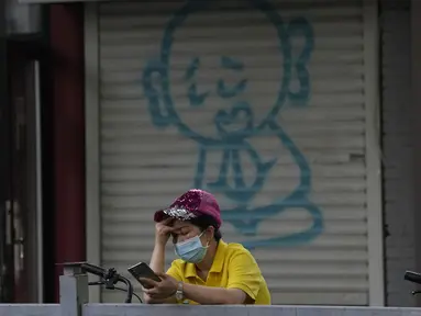 Seorang wanita melihat teleponnya di dekat grafiti yang menggambarkan seorang biarawan di Beijing (24/5/2022). Beijing memperpanjang perintah bagi pekerja dan pelajar untuk tinggal di rumah dan memerintahkan pengujian massal tambahan pada Senin ketika kasus COVID-19 meningkat di ibu kota China. (AP Photo/Ng Han Guan)