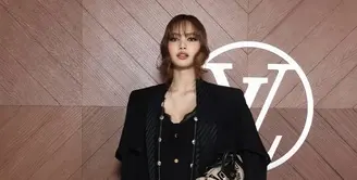 Lisa Blackpink hadir dengan gaya serba hitam mengenakan coat panjang dengan inner jumpsuit berkancing gold dipadukan kalung panjang tanpa liontin dan sepatu boots heels hitam. Ia membawa handbag warna coklat. [dok. Louis Vuitton]