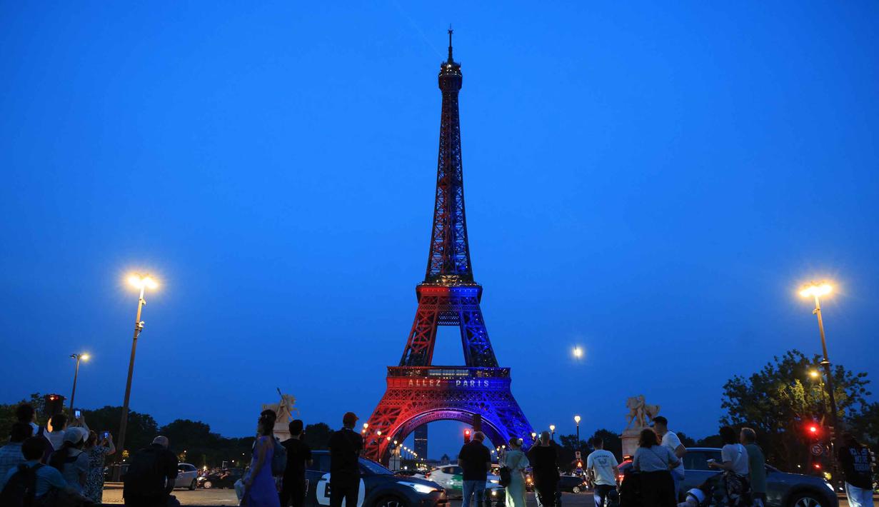 Orang-orang memandang Menara Eiffel yang diterangi cahaya warna-warna khas, dengan pesan bertuliskan "Allez Paris" ("Ayo, Paris"), pada malam menjelang pertandingan final Liga Champions 2025/2026 antara Paris Saint-Germain (PSG) dan Arsenal, Kamis 29 Mei 2026. (Ludovic MARIN/AFP)