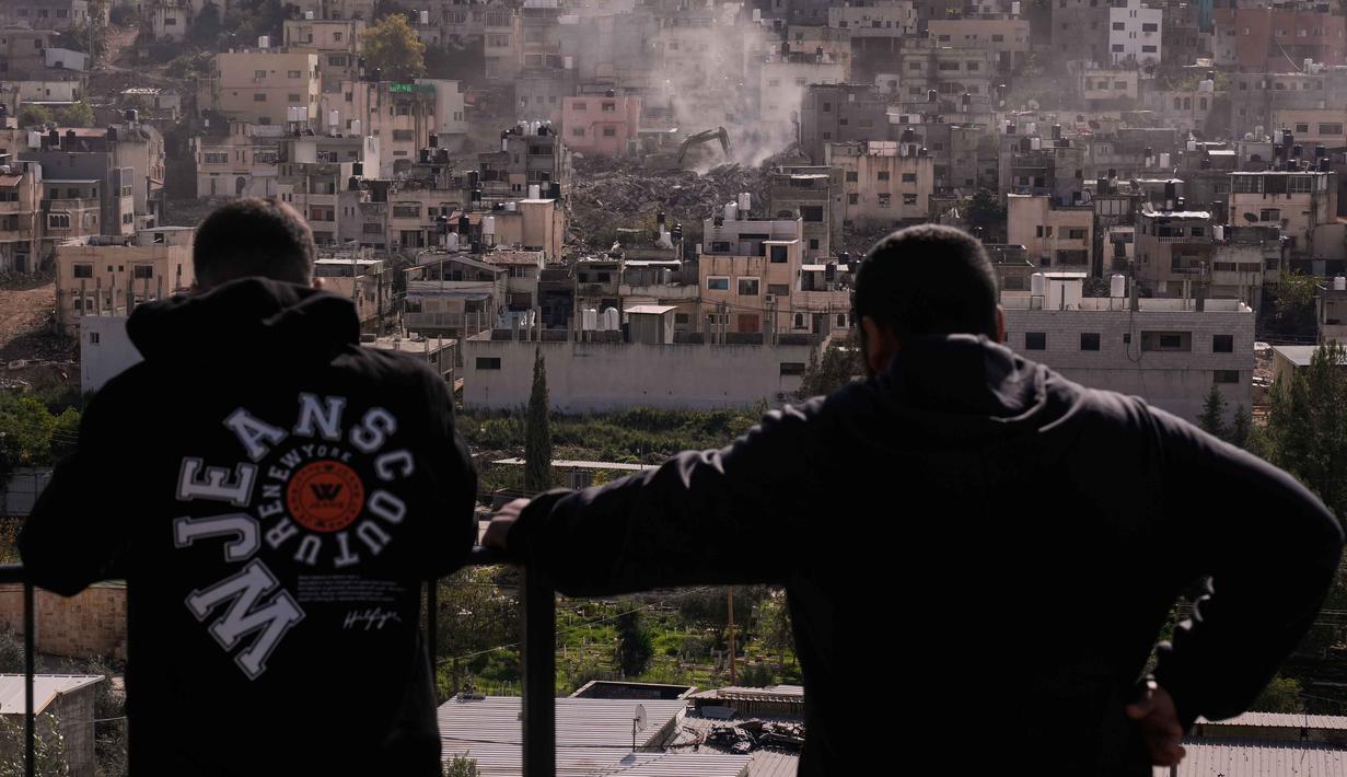 Pembongkaran juga ditujukan untuk menghancurkan infrastruktur militan di wilayah Tepi Barat bagian utara. Tampak dalam foto, warga menyaksikan buldoser tentara Israel merobohkan rumah-rumah di kamp pengungsi perkotaan Palestina Nur Shams, dekat kota Tulkarem di Tepi Barat, Rabu 31 Desember 2025. (AP Photo/Majdi Mohammed)