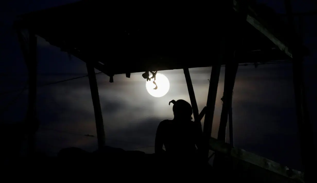 Seorang wanita duduk di teras atap rumahnya melihat fenomena Supermoon di Port-au-Prince, Haiti (13/11). Fenomena ini merupakan bulan paling besar dan terang dalam kurun 70 tahun terakhir. (REUTERS/Andres Martinez Casares)