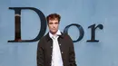 Robert Pattinson kenakan jaket bomber wol coklat Dior, kemeja katun bergaris, dan dasi sutra. Dipadu celana panjang lipit krem, dan sepasang sepatu kets suede coklat dan coklat. [Dior]