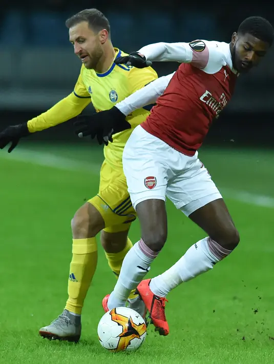 Gelandang BATE Borisov, Ihor Stasevich (berebut bola dengan pemain Arsenal, Ainsley Maitland-Niles pada leg pertama 32 besar Liga Europa di Borisov Arena, Kamis (14/2). Arsenal kalah 0-1 saat bertandang ke markas Bate Borisov. (Sergei GAPON / AFP)
