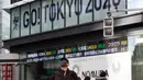 Seorang pria yang mengenakan masker berjalan dekat papan bertema Olimpiade yang disponsori perusahaan sekuritas di Tokyo, Jepang, Jumat (29/1/2021). Olimpiade 2020 Tokyo yang ditunda terkait pandemi virus corona Covid-19 dijadwalkan ulang untuk diadakan pada musim panas ini. (AP Photo/Hiro Komae)