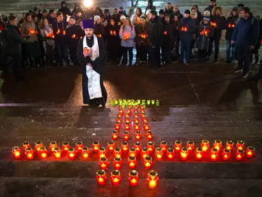 Warga dengan seorang imam berkumpul di Katedral Kristus Juruselamat Moskow, Rusia, Senin (12/2). Mereka menyalakan lilin untuk mengenang 71 korban tewas kecelakaan pesawat Rusia di Moskow. (AP Photo / Alexander Zemlianichenko)
