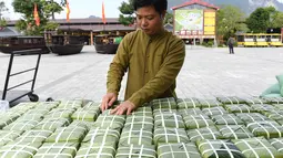Seorang pria sedang mengatur paket "Banh Chung" atau kue beras tradisional Vietnam untuk amal, menjelang Tahun Baru Imlek atau festival Tet di Pagoda Tam Chuc di provinsi Ha Nam (7/1/2023). Banh Chung adalah kelezatan khas Vietnam yang terbuat dari ketan, daging babi, dan kacang hijau yang dibungkus dengan daun pisang dan dimasak selama 10 jam. (AFP/Nhac Nguyen)