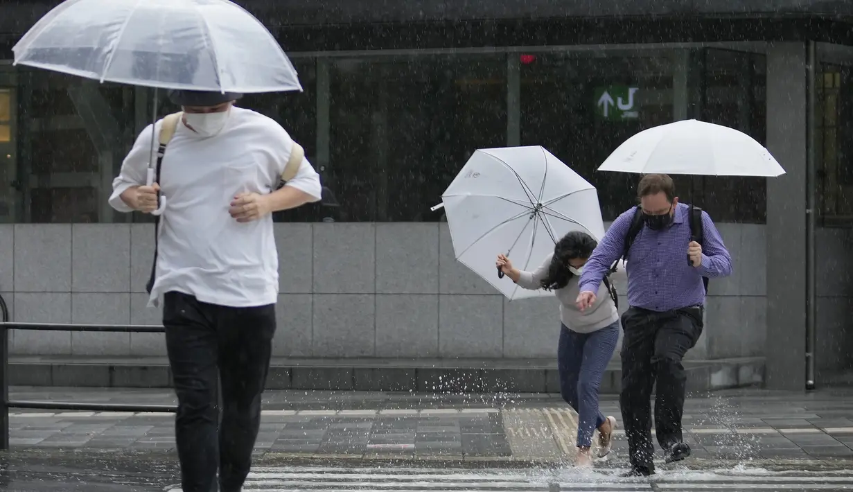 Orang-orang mengarungi genangan air saat mereka berjalan melintasi persimpangan di tengah hujan di Tokyo, Selasa (20/9/2022). Sebanyak dua orang dilaporkan tewas dan 100 orang lainnya akibat badai yang melumpuhkan lalu lintas, dan membuat ribuan rumah tanpa aliran listrik.  (AP Photo/Hiro Komae)