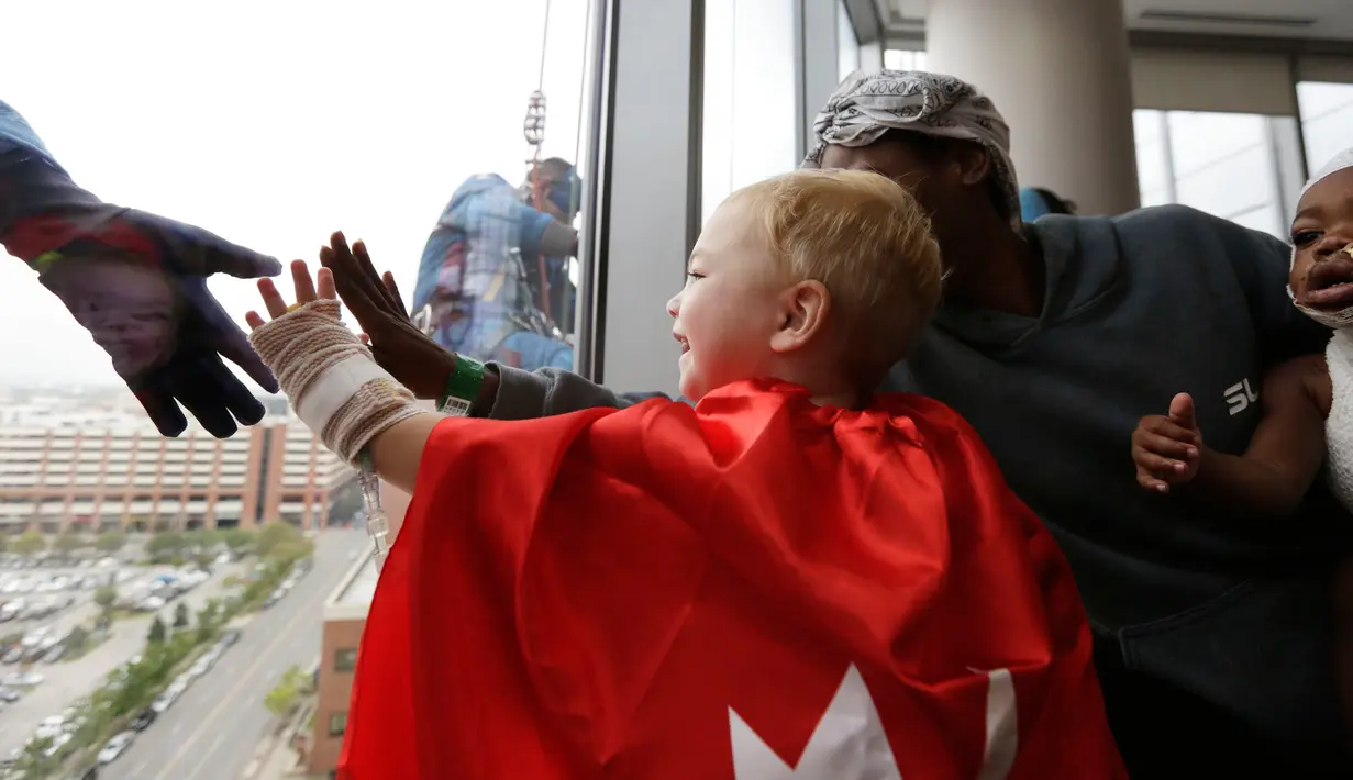 Pasien anak berusaha menyentuh tangan superhero Superman yang membersihkan kaca jendela kamar di sebuah rumah sakit di Birmingham, Rabu (11/10). Para pekerja bergelantungan di luar jendela dengan mengenakan kostum superhero. (AP Photo/Brynn Anderson)