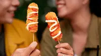 Dua orang sedang menunjukkan kuliner kekinian corndog sosis (Sumber: Freepik)