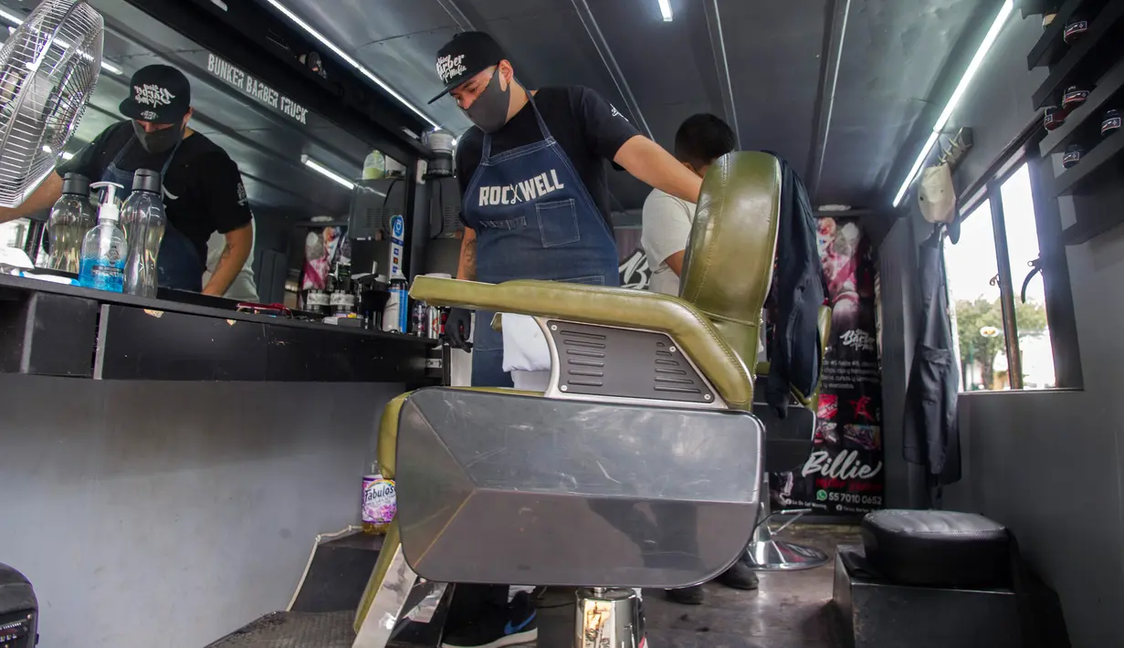 Seorang tukang cukur terlihat di dalam mobil van atau truck yang diubah menjadi barbershop di sebuah jalan di tengah pandemi virus corona COVID-19, di Mexico City, pada Minggu (6/9/2020). (Photo by CLAUDIO CRUZ / AFP)