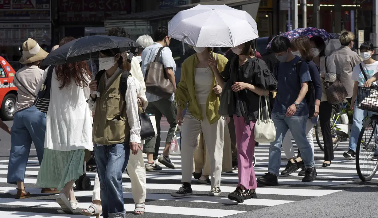 Orang-orang berjalan di atas penyeberangan pejalan kaki di bawah terik matahari di Tokyo, Senin (30/5/2022). Cuaca panas pada hari Senin telah ditetapkan dengan suhu naik lebih dari 27 derajat Celcius (80,6 derajat Fahrenheit) di Tokyo, menurut Badan Meteorologi Jepang. (AP Photo/Eugene Hoshiko)