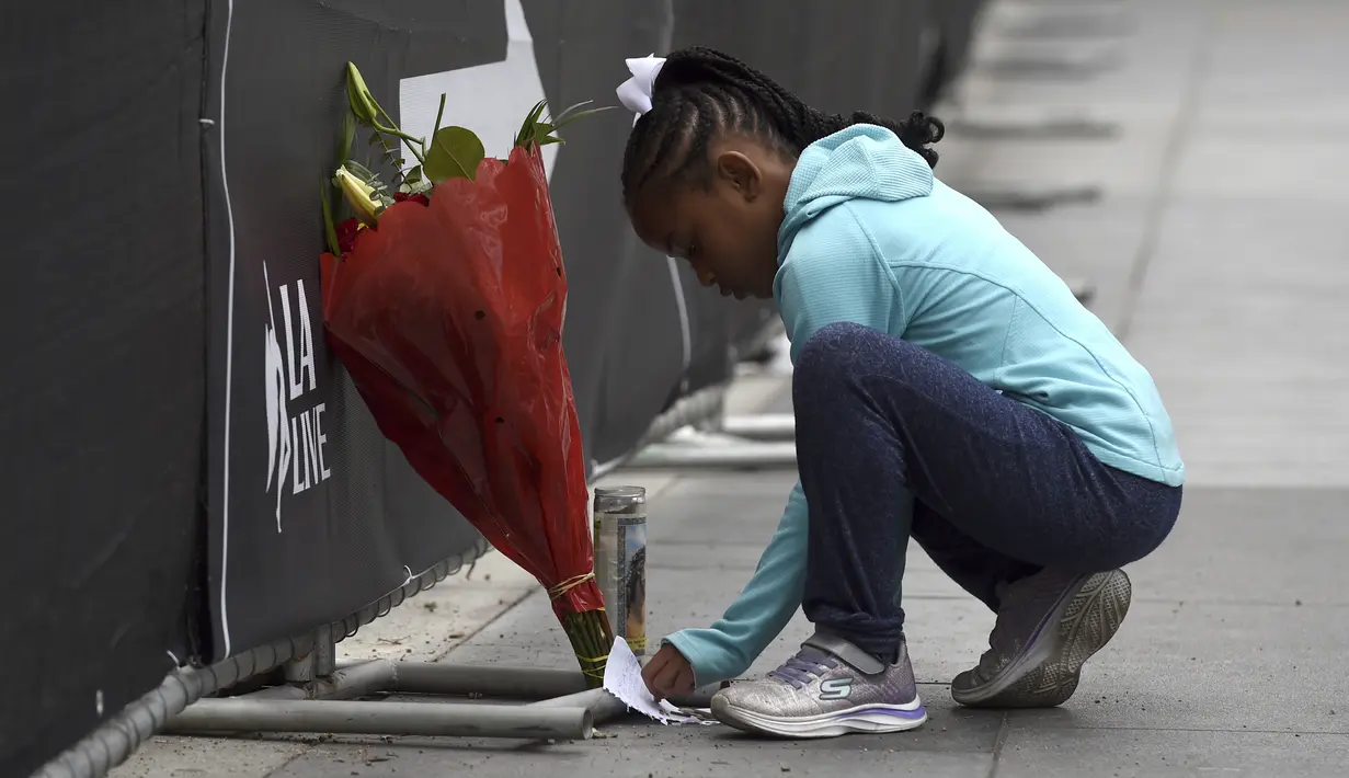 Dharma Brown (8) dari Los Angeles menulis catatan untuk mendiang Kobe Bryant di luar Staples Center, Los Angeles (26/1/2020). Kobe Bryant dan Gianna terbang menggunakan helikopter untuk mengikuti latihan basket di Mamba Academy. (AP Photo/Chris Pizzello)