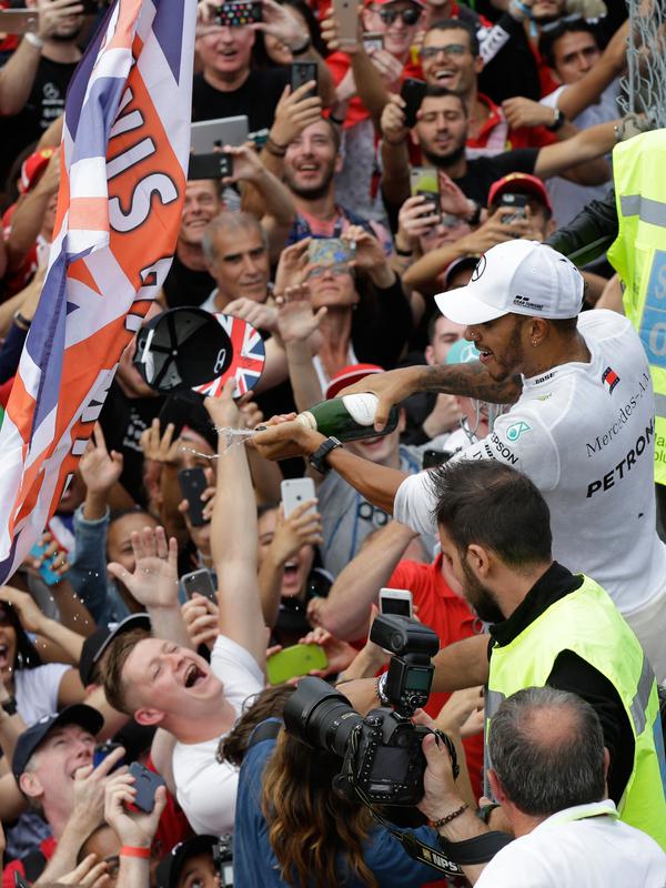 Pembalap Mercedes, Lewis Hamilton menyemprotkan sampanye ke pendukungnya saat merayakan keberhasilannya memenangkan GP Italia di Sirkuit Monza di Monza, Italia, (2/9). (AP Photo/Luca Bruno)