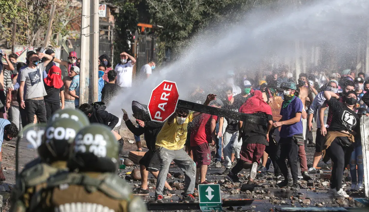 Demonstran saat bentrok dengan polisi di lingkungan miskin di Santiago, Chili, (18/5/2020). Pemerintah sebenarnya sudah mendistribusikan 2.000 paket bantuan kepada keluarga di area tersebut. Namun bantuan diberikan hanya kepada yang paling membutuhkan. (AP Photo/Esteban Felix)