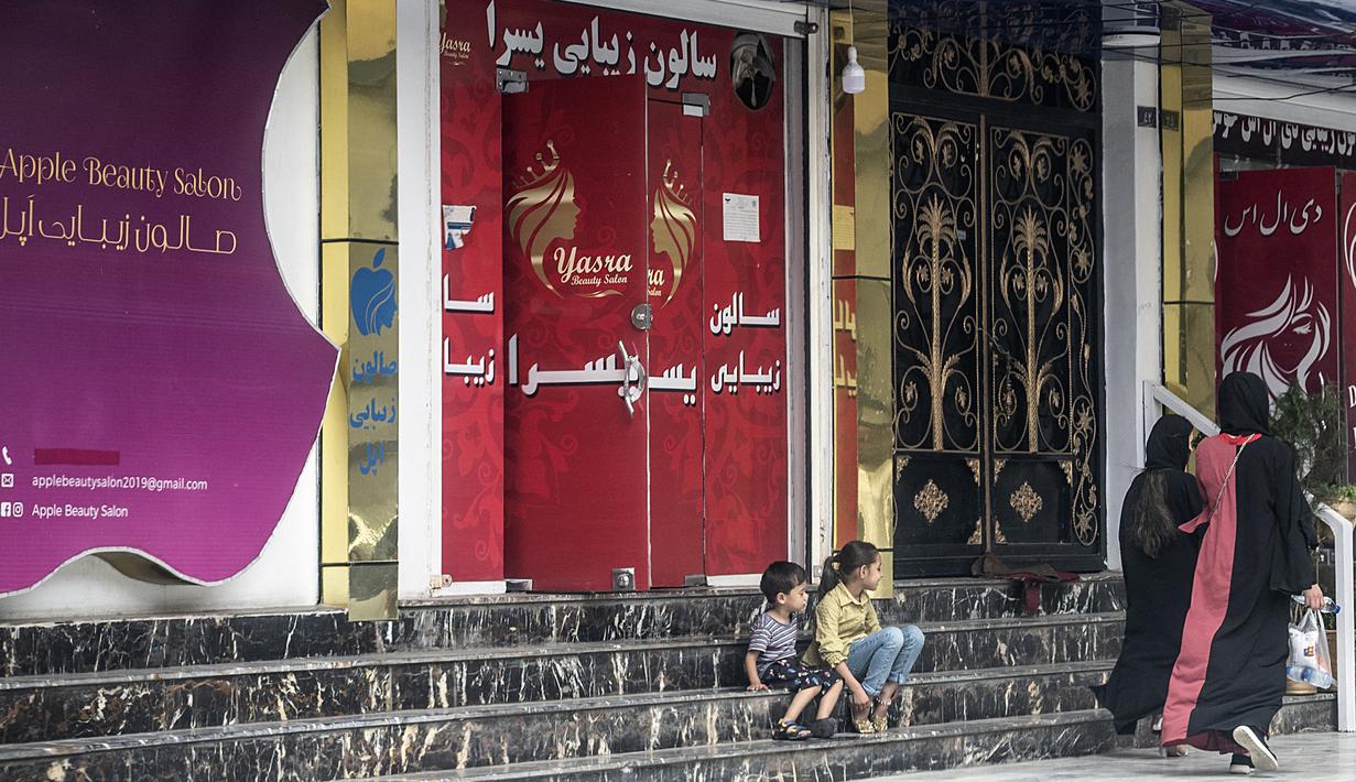 Perempuan berjalan melewati salon kecantikan di daerah Shahr-e Naw di Kabul, Afghanistan pada Selasa (4/7/2023). (Photo by Wakil KOHSAR / AFP)