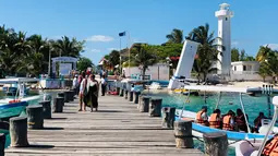 Turis berjalan di sepanjang dermaga di Puerto Morelos, negara bagian Quintana Roo, Meksiko (14/2). Puerto Morelos dibagi oleh jalan raya dan rawa bakau menjadi tiga bagian. (AFP Photo/Daniel Slim)