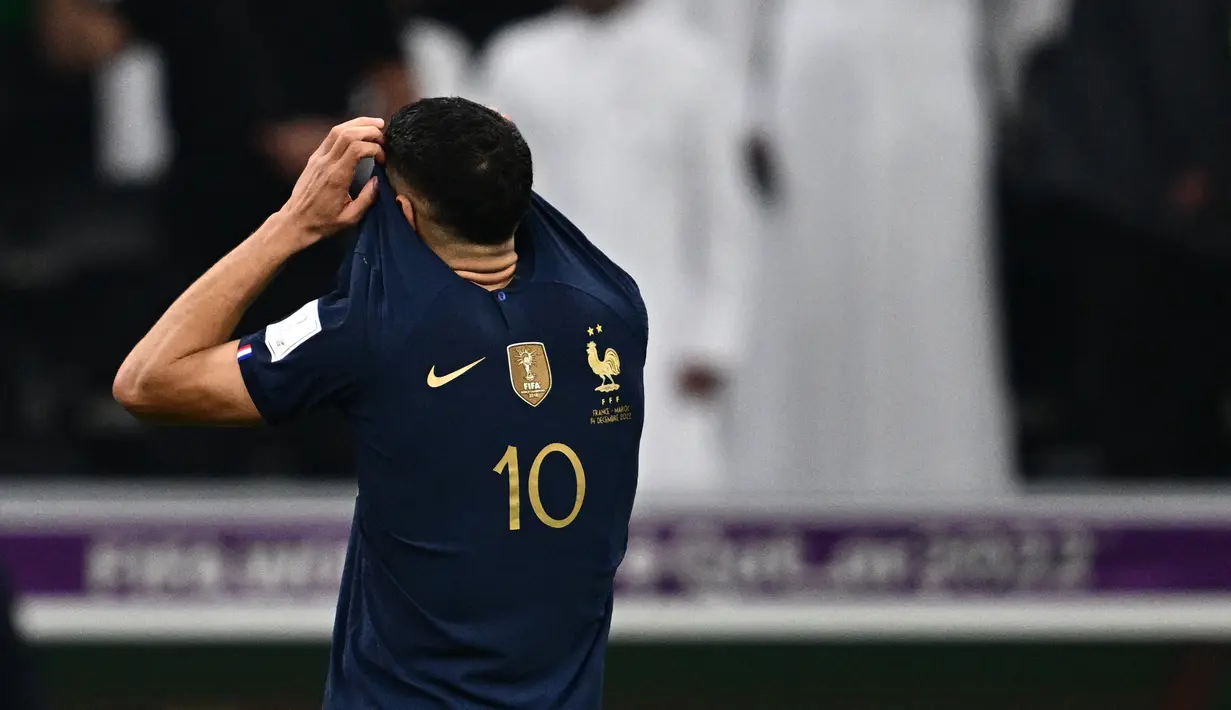 Bek Maroko Achraf Hakimi menutupi wajahnya dengan jersey penyerang Prancis Kylian Mbappe setelah pertandingan semifinal Piala Dunia 2022 di Stadion Al-Bayt di Al Khor, Doha, Kamis (15/12/2022). Maroko gagal melaju ke final Piala Dunia 2022 Qatar setelah kalah dari Prancis dengan skor 2-0. (AFP/Gabriel Bouys)