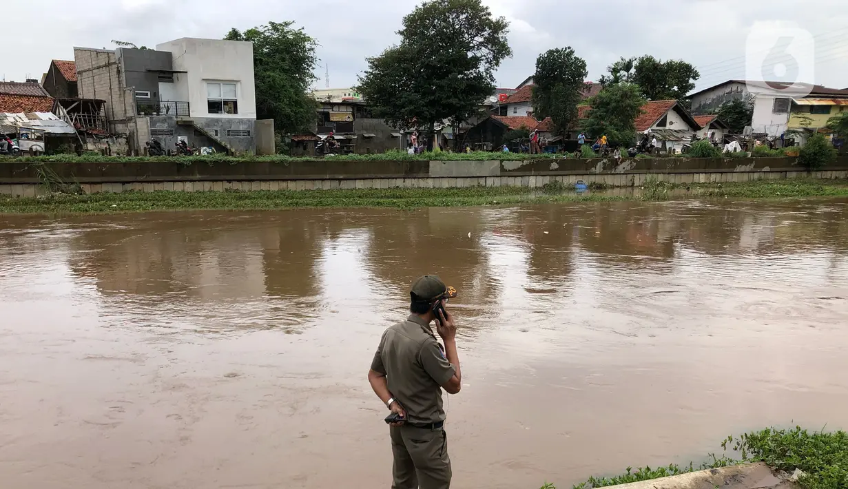 Petugas berdiri di bantaran Sungai Ciliwung di kawasan Rawajati,  Jakarta, Selasa (25/2/2020). Adanya seorang warga yang hanyut saat berenang di tengah luapan Sungai Ciliwung tersebut mengundang perhatian warga serta petugas yang mencari keberadannya. (Liputan6.com/Immanuel Antonius)