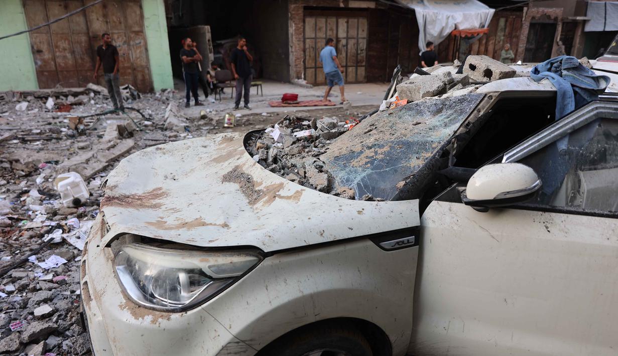 Orang-orang berdiri di tengah reruntuhan bangunan tempat tinggal dan sebuah mobil yang rusak setelah serangan Israel di Kota Gaza pada Kamis 4 Juni 2026. (Omar AL-QATTAA/AFP)