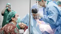 Pada foto lain, seorang dokter memegangi bayi. Dokter berbaju dinas lengkap plus sarung tangan dan penutup kepala memperlihatkan bayi yang baru lahir kepada Gya Sadiqah dan Tarra Budiman. Gya yang mengenakan alat bantu napas tersenyum semringah melibat putri keduanya. Sementara Tarra Budiman yang pakai masker tampak bahagia. Matanya berbinar melihat si kecil. (Foto: Bukaan Moment dari Instagram @gyaps)