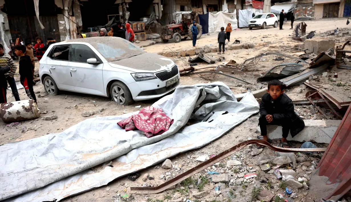Sementara, Hamas membantah keras klaim tersebut. Hamas menilai alasan yang disampaikan Israel sebagai dalih untuk membenarkan serangan mematikan terhadap warga sipil di Jalur Gaza. Tampak dalam foto, seorang anak laki-laki Palestina yang mengungsi duduk di atas reruntuhan setelah pesawat Israel menargetkan sebuah rumah berlantai lima tadi malam, di Khan Yunis, Jalur Gaza selatan, pada Kamis 6 Februari 2026. (Bashar Taleb/AFP)